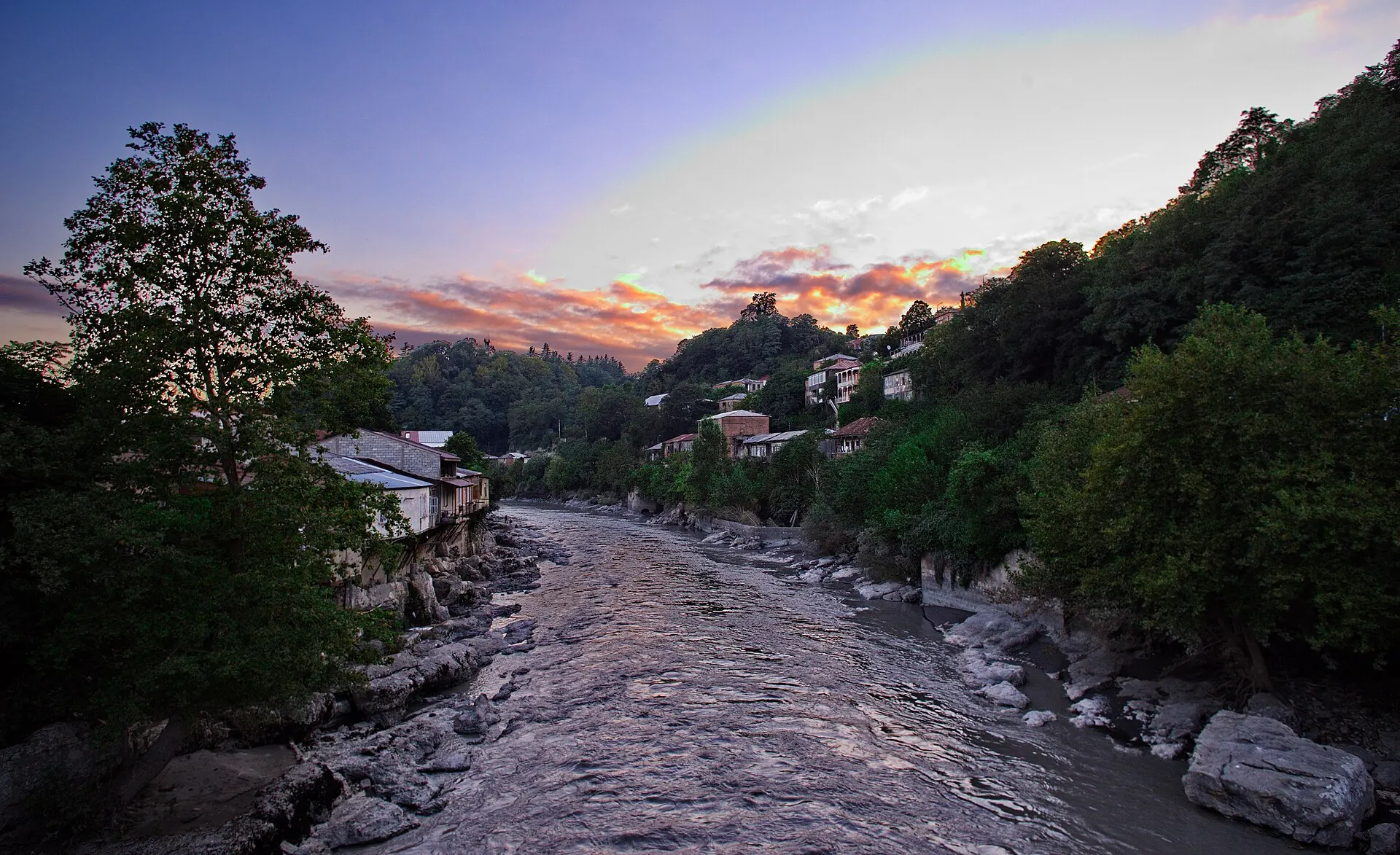 Rioni River between wooded banks and houses at sunset in Kutaisi