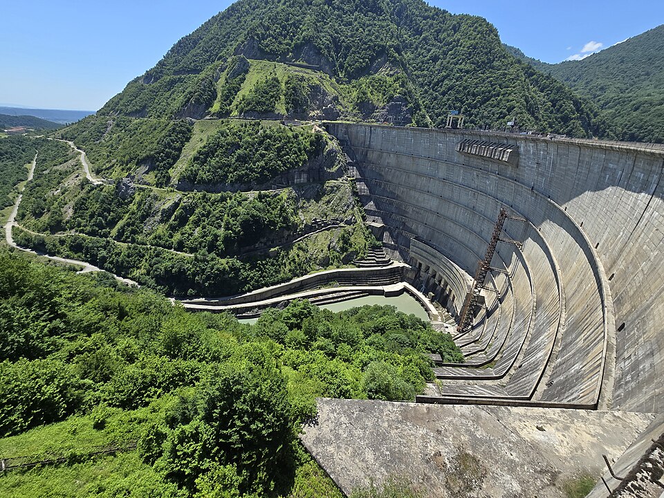 Curving concrete wall of the Enguri arch dam among green hills