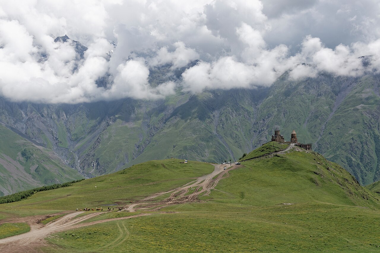 Gergeti Trinity Church on a green ridge beneath clouded Caucasus mountains