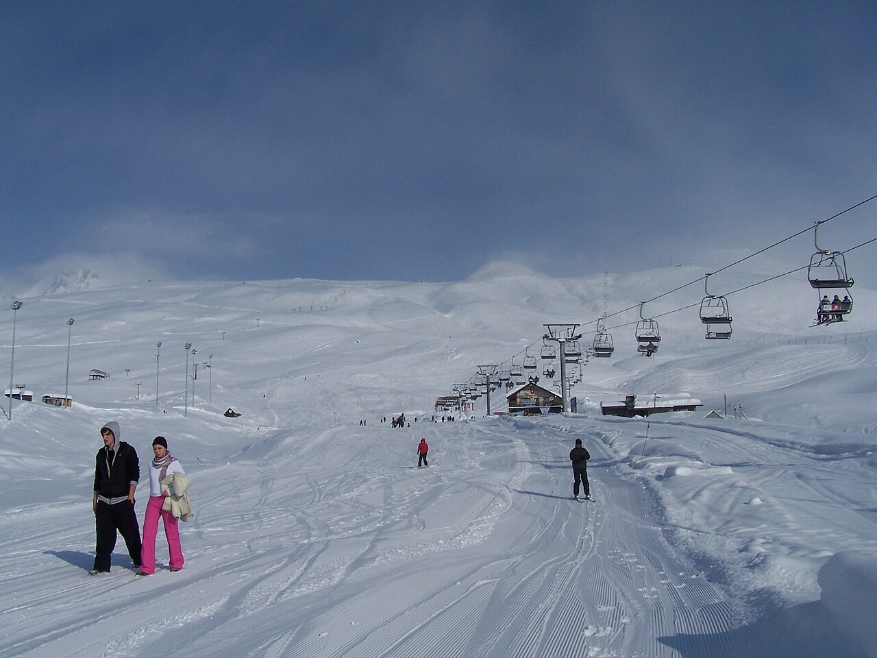 Skiers on a marked snowy run beside a chairlift at Gudauri