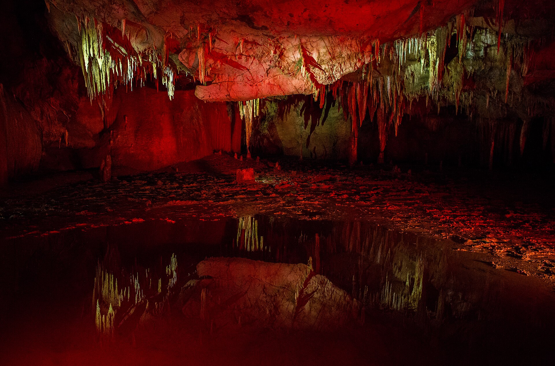 Illuminated stalactites reflected in a still pool inside Prometheus Cave
